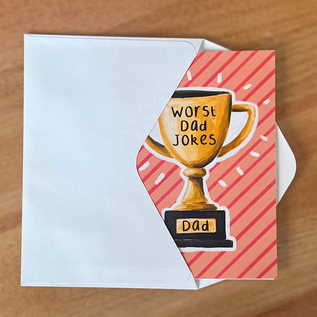 Father’s Day card with a trophy illustration and text 'Worst Dad Jokes' on a wooden surface