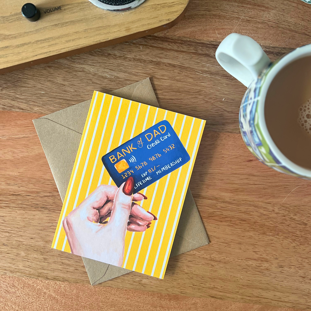 Fathers day card with a bank card design on a wooden surface with a mug.