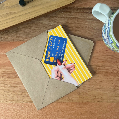 Father’s Day card tucked into an envelope on a wooden surface with a mug to the side.