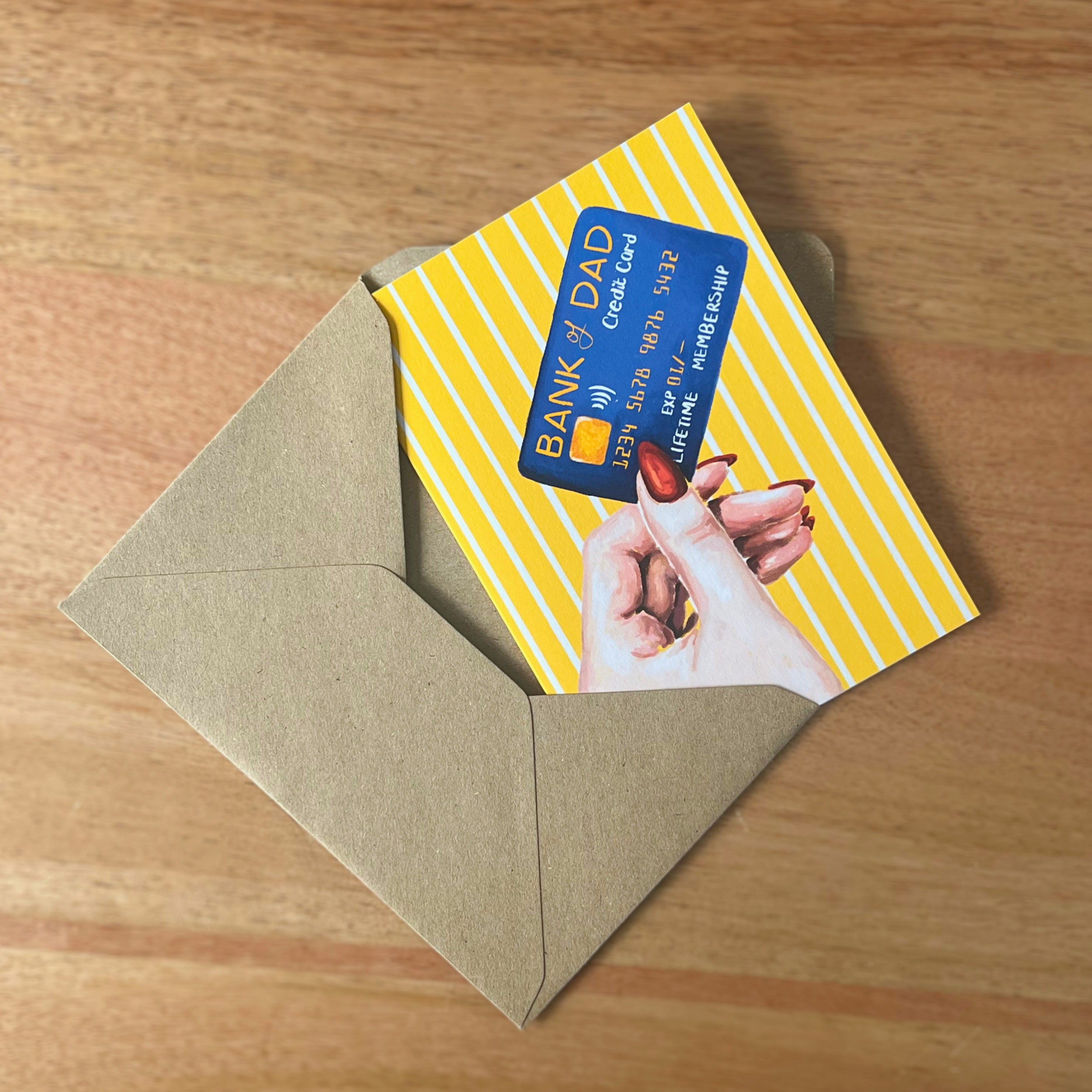 Father’s Day Card with 'Bank of Dad' design inside an open envelope on a wooden surface