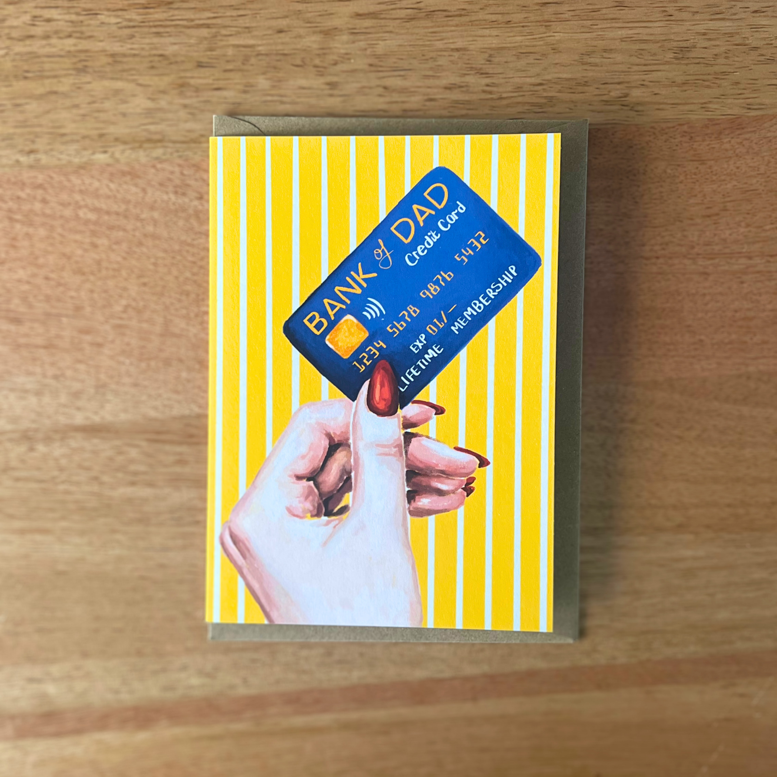 Fathers day card with a hand holding a blue card against a yellow striped background on a wooden surface