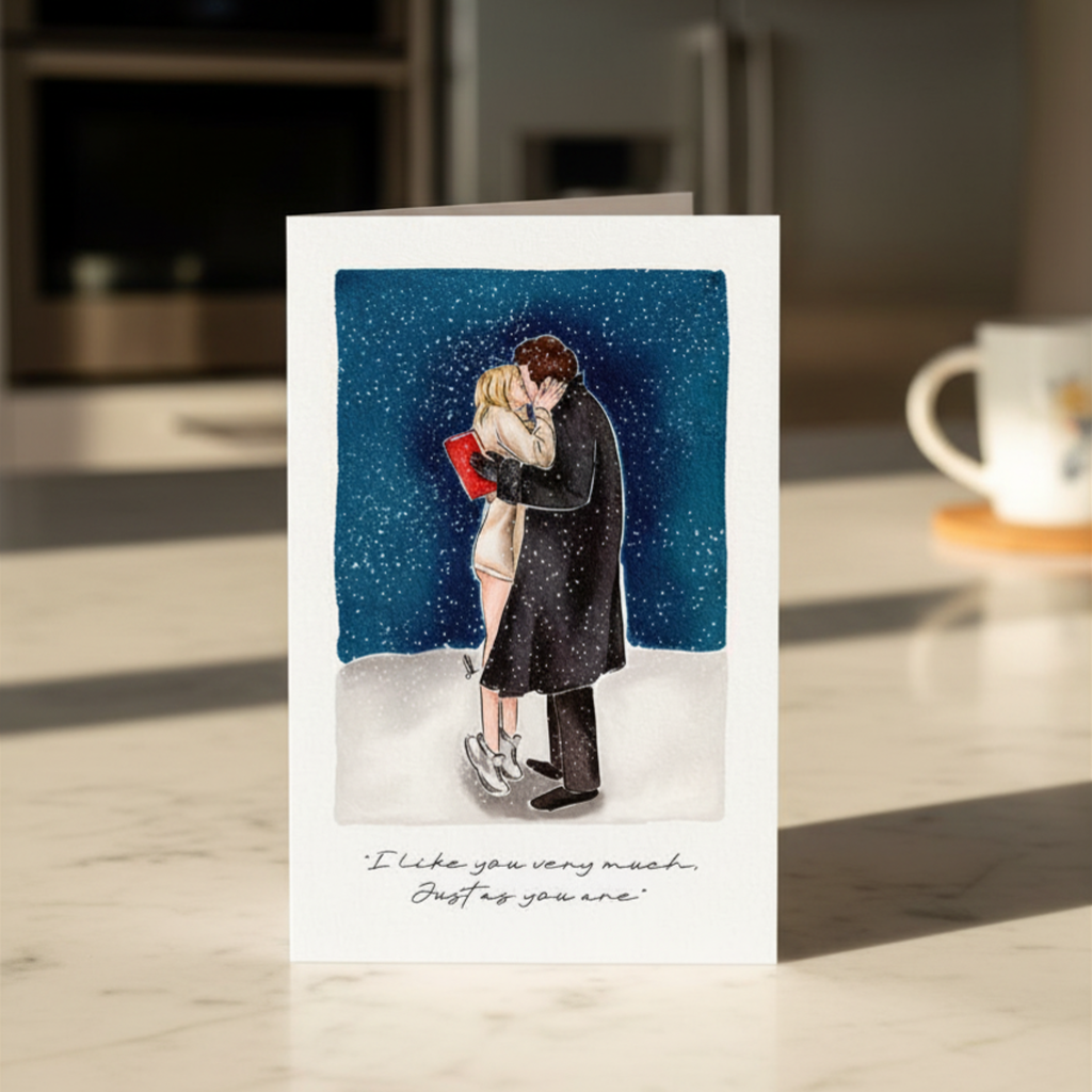 Greeting card with illustration of a couple kissing in the snow with a quote beneath, placed on a kitchen surface.