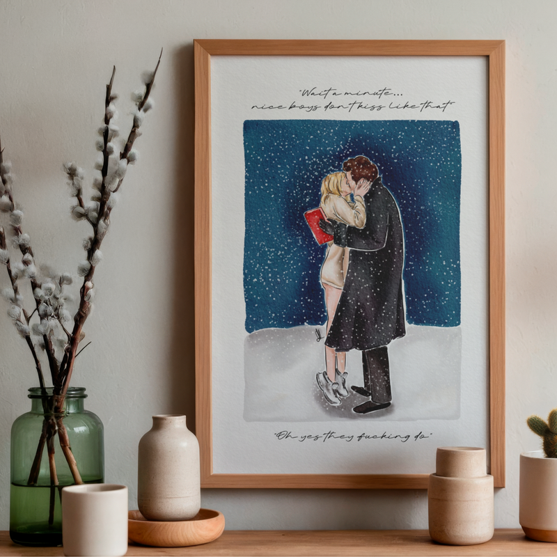 Art print of couple kissing in the snow with a quote saying ‘wait a minute, nice boys don’t kiss like that’ and ‘oh yes they fucking do’ Styled in a frame