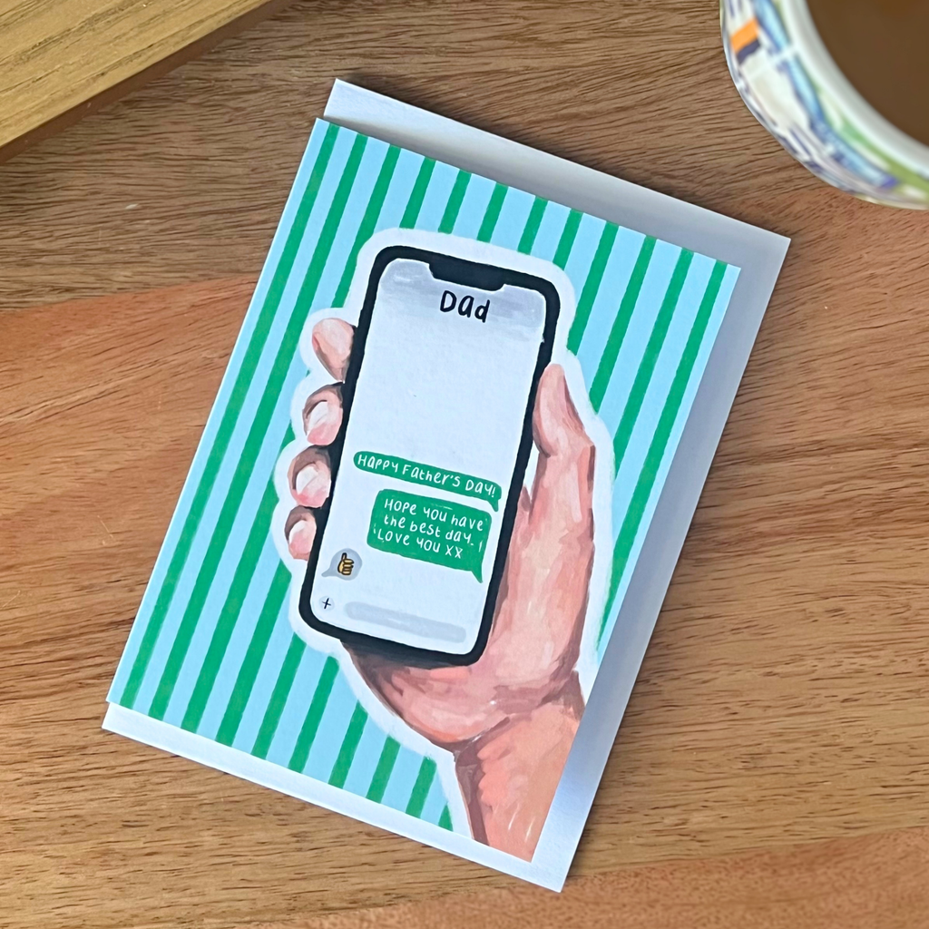 Greeting card with a hand holding a phone on a striped background, placed on a wooden surface.