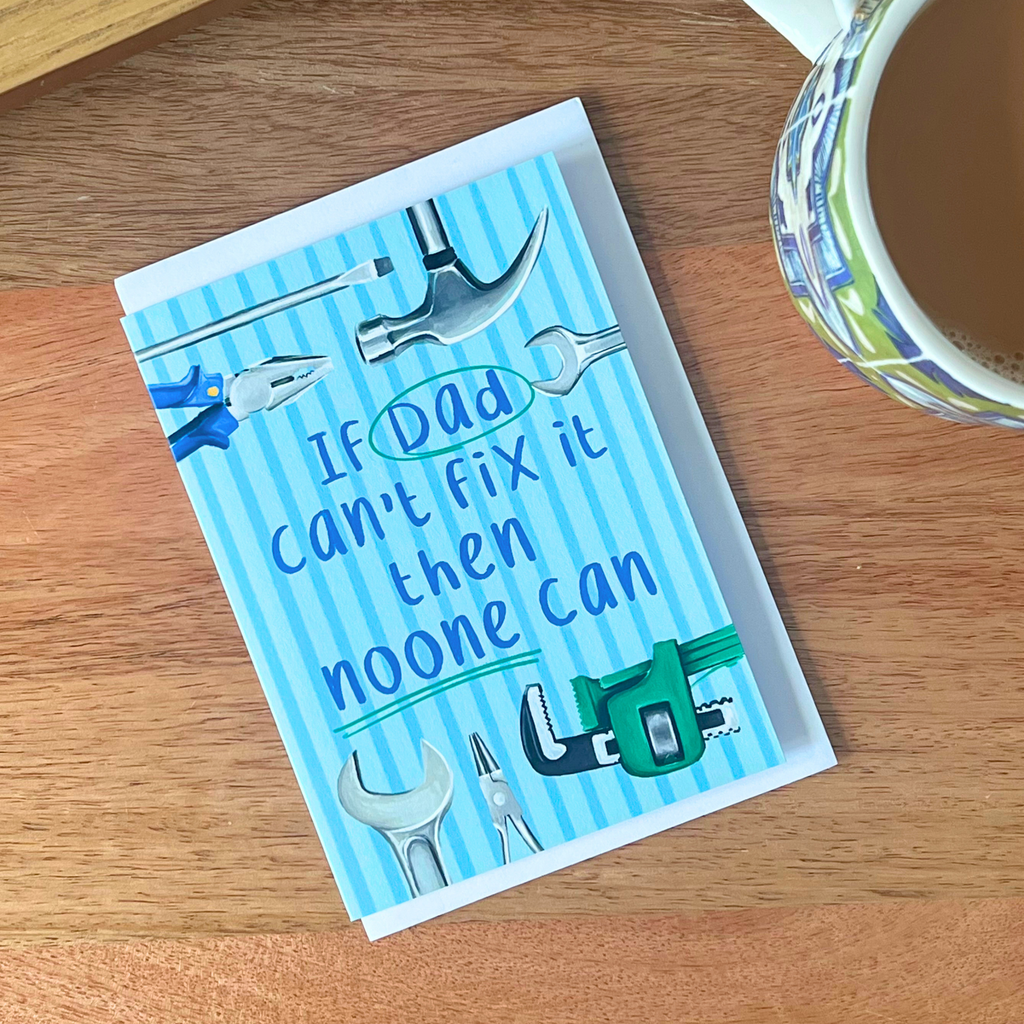 Fathers day card with tools and humorous text on a wooden surface with a cup of coffee.