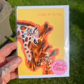 Greeting card with giraffe illustration held by a hand on grass