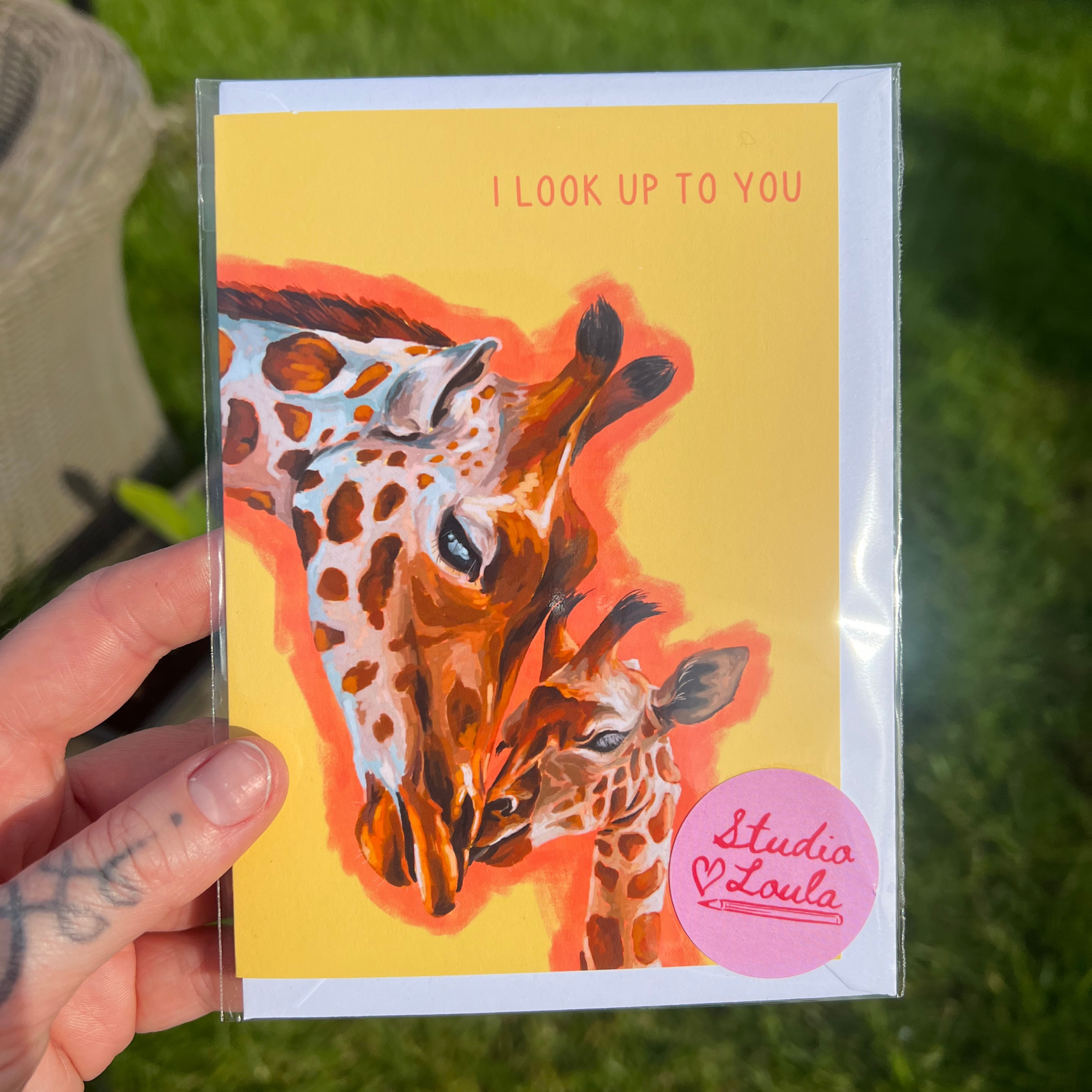 Greeting card with giraffe illustration held by a hand on grass