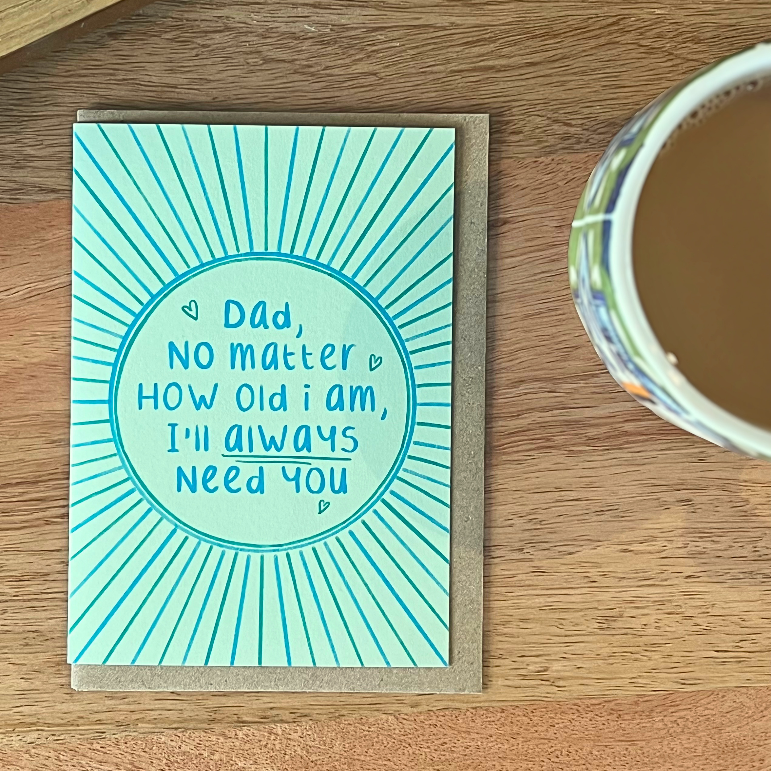 Father’s Day card with ‘dad no matter how old i am ill always need you’ message on a wooden surface next to a cup of coffee