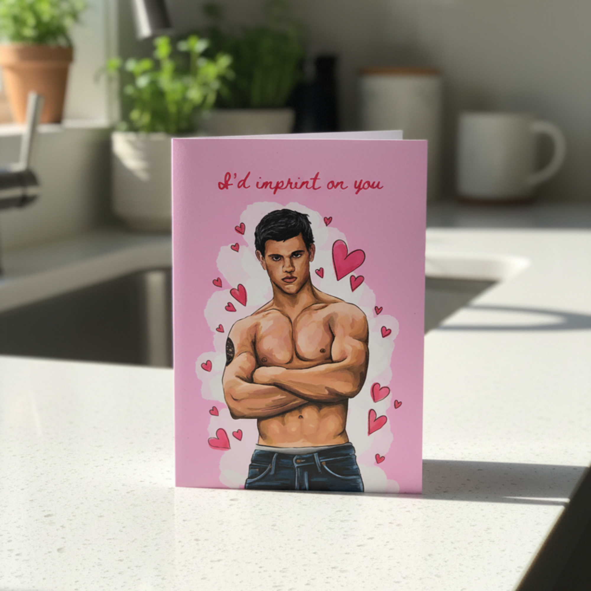 Card with a muscular man illustration and I’d imprint on you text on a pink background, placed in a kitchen.