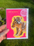 Card with a tiger cub illustration and 'Love You Bestie' text, held in front of grass.