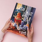 Art print of a woman reading in bed by a window with 'Late Night Reading Club' text, held against a pink background