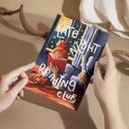 Art print of a woman reading in bed by a window with 'Late Night Reading Club' text, held against a neutral background