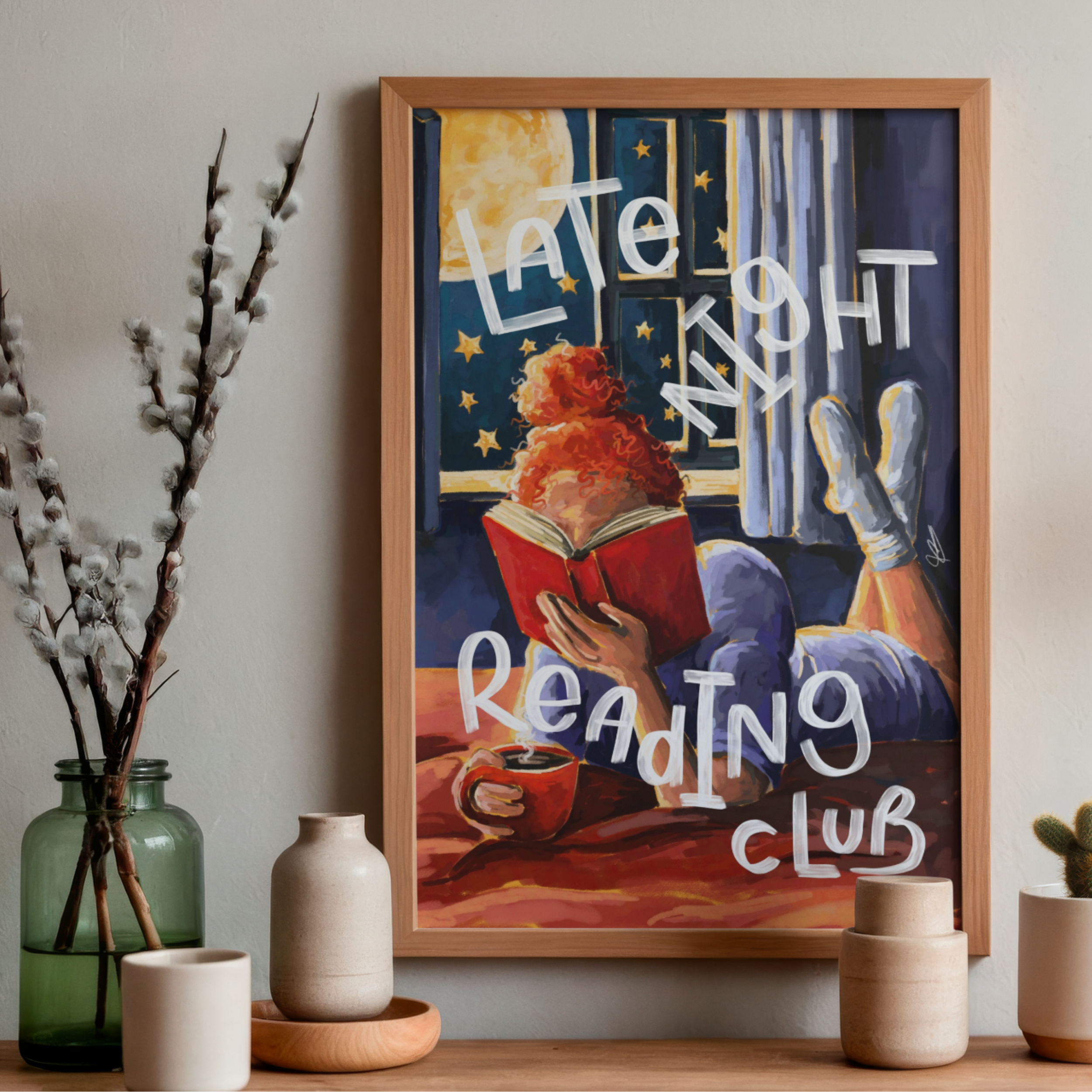 Framed art print of a woman reading in bed by a window with 'Late Night Reading Club' text, hung on a wall