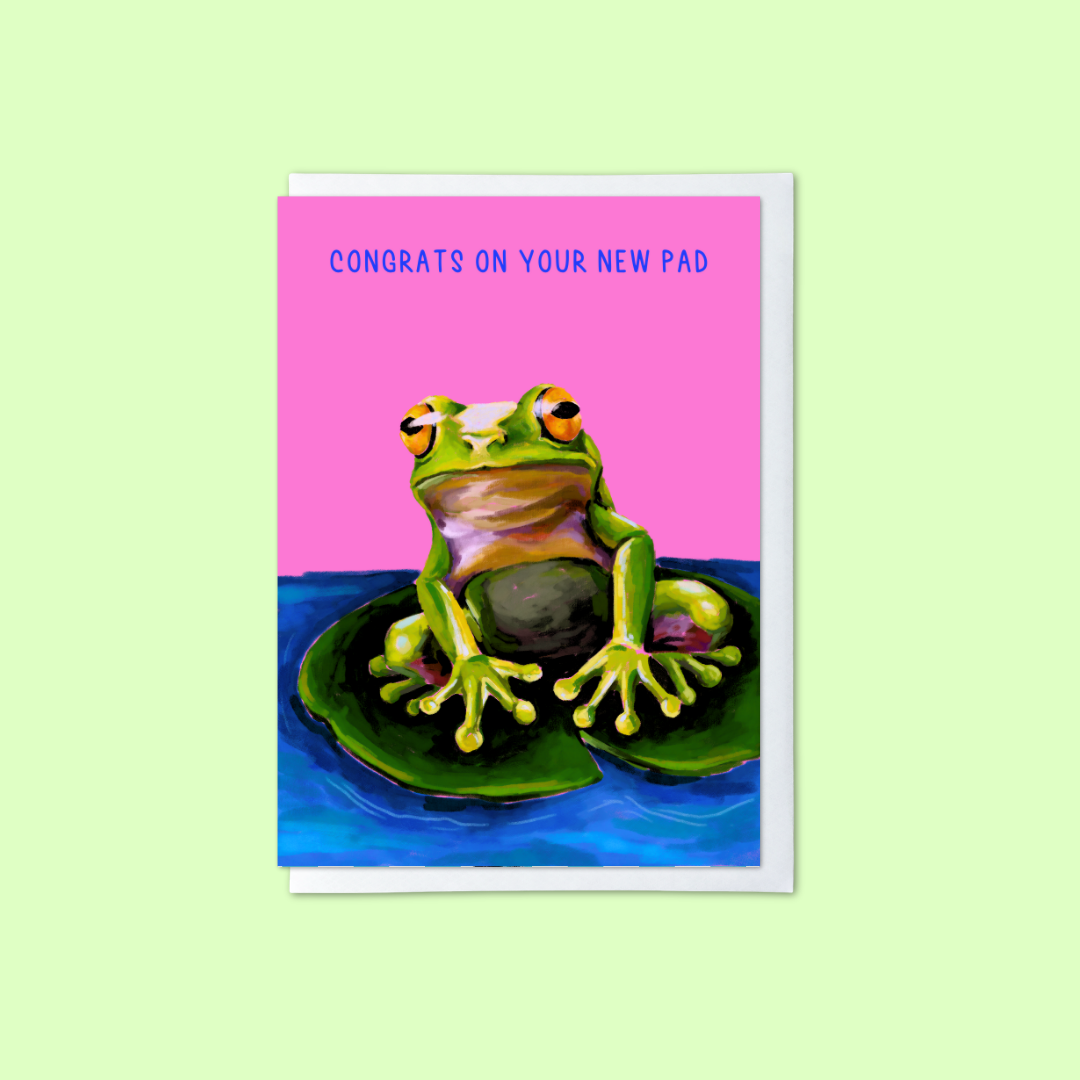 Pink greeting card with frog on a lily pad illustration and ‘congrats on your new pad’ message on a green background