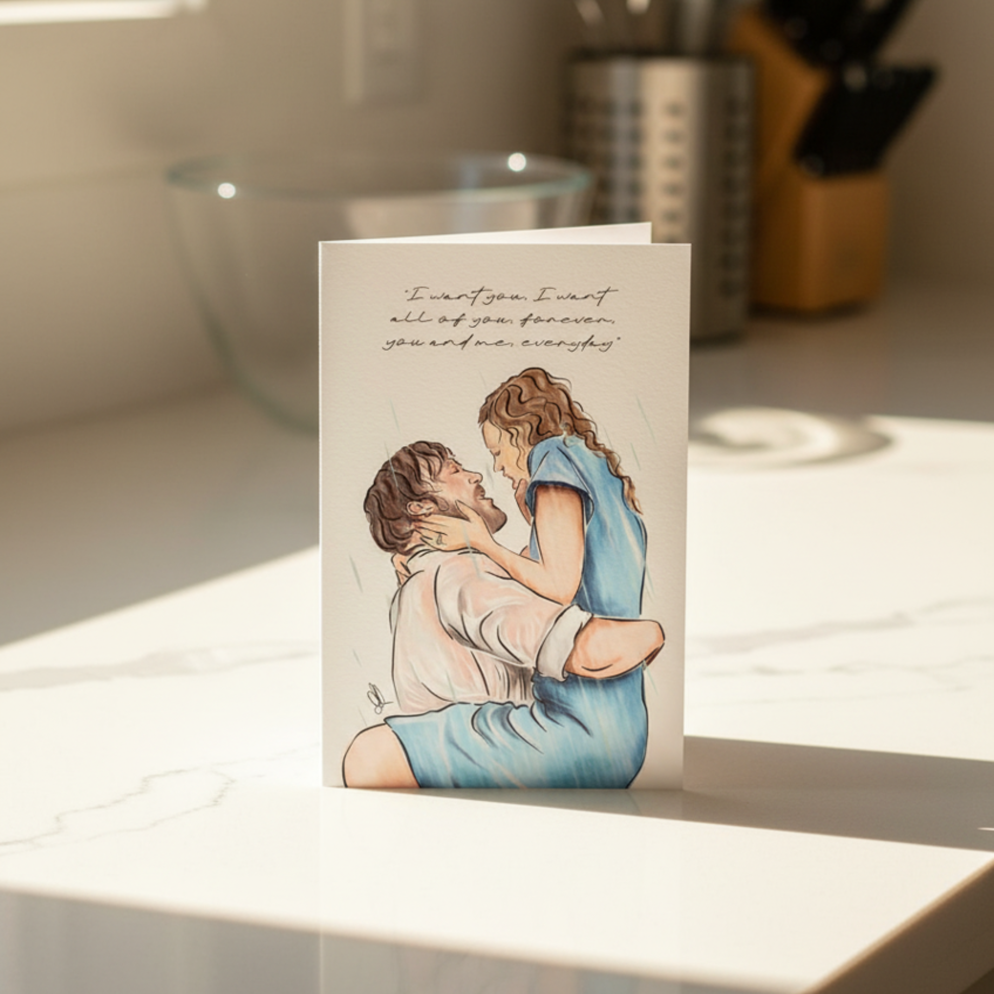 Greeting card with illustration of a couple kissing in the rain with quote above, on a kitchen counter