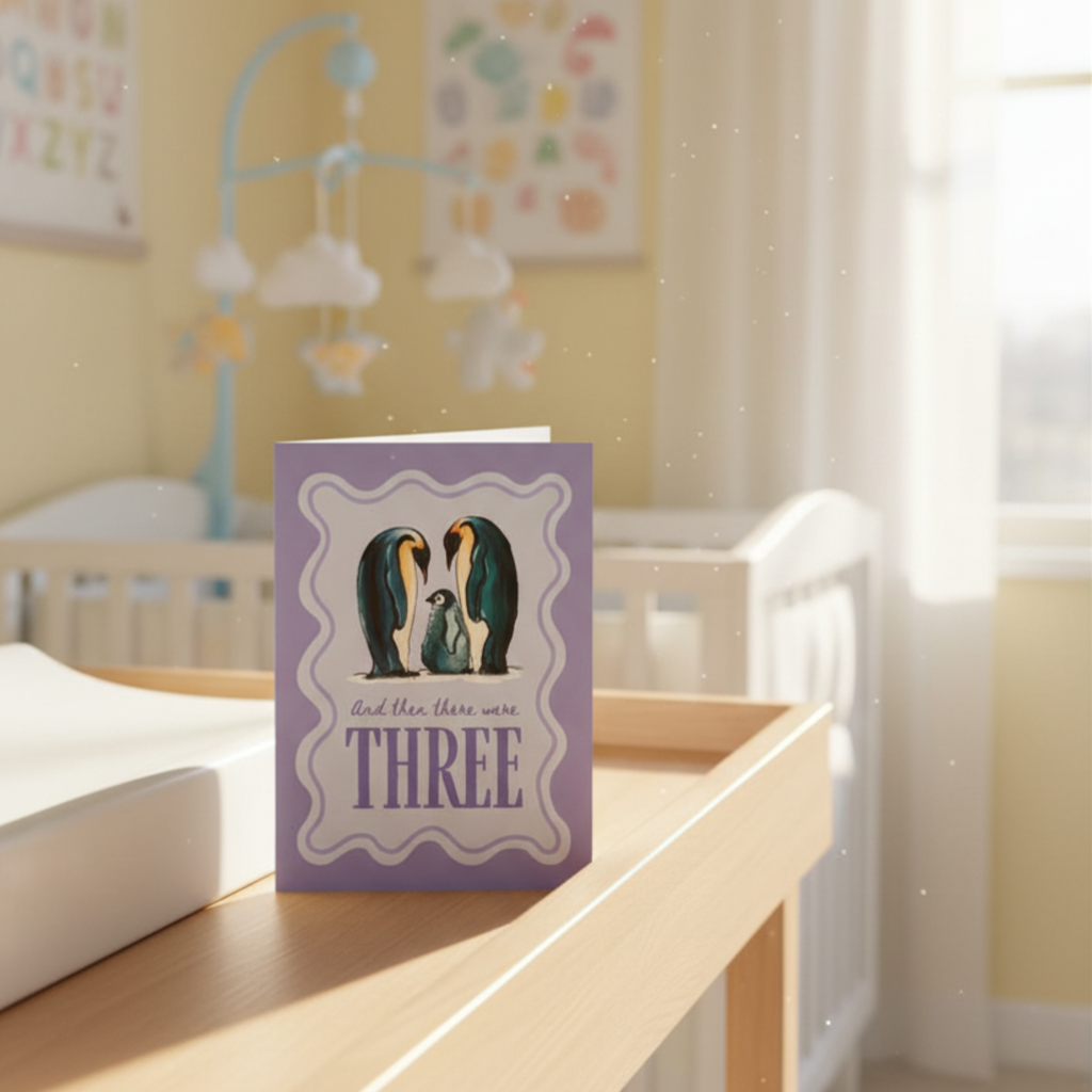 Purple card with penguin family design and ‘and then there were three’ text in a nursery