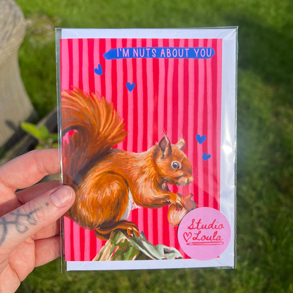 Card with a squirrel illustration and 'I'm nuts about you' text held by a hand on grass.