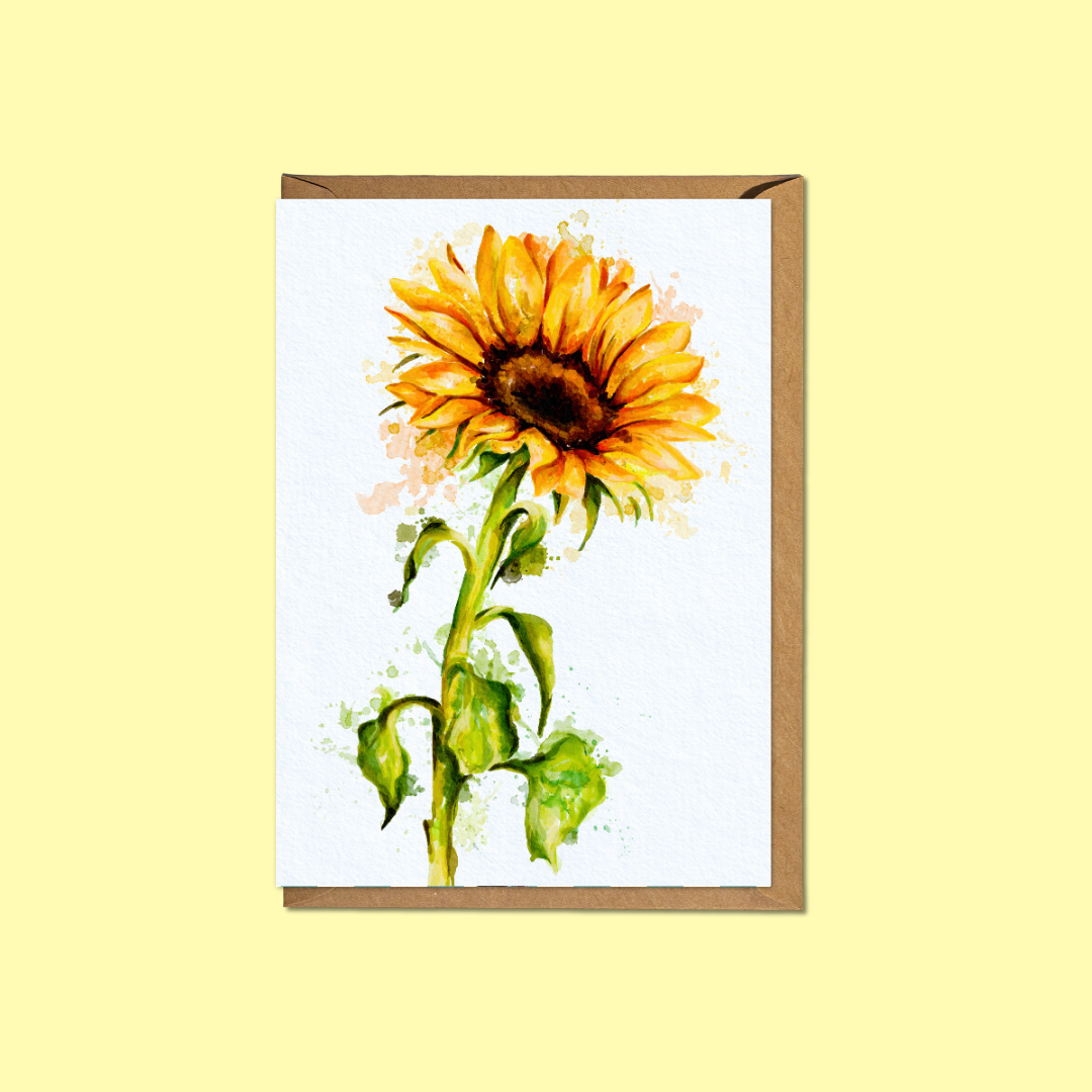 A vertical greeting card featuring a watercolor-style sunflower illustration on a white background, shown with a brown kraft envelope behind it against a pale yellow backdrop.