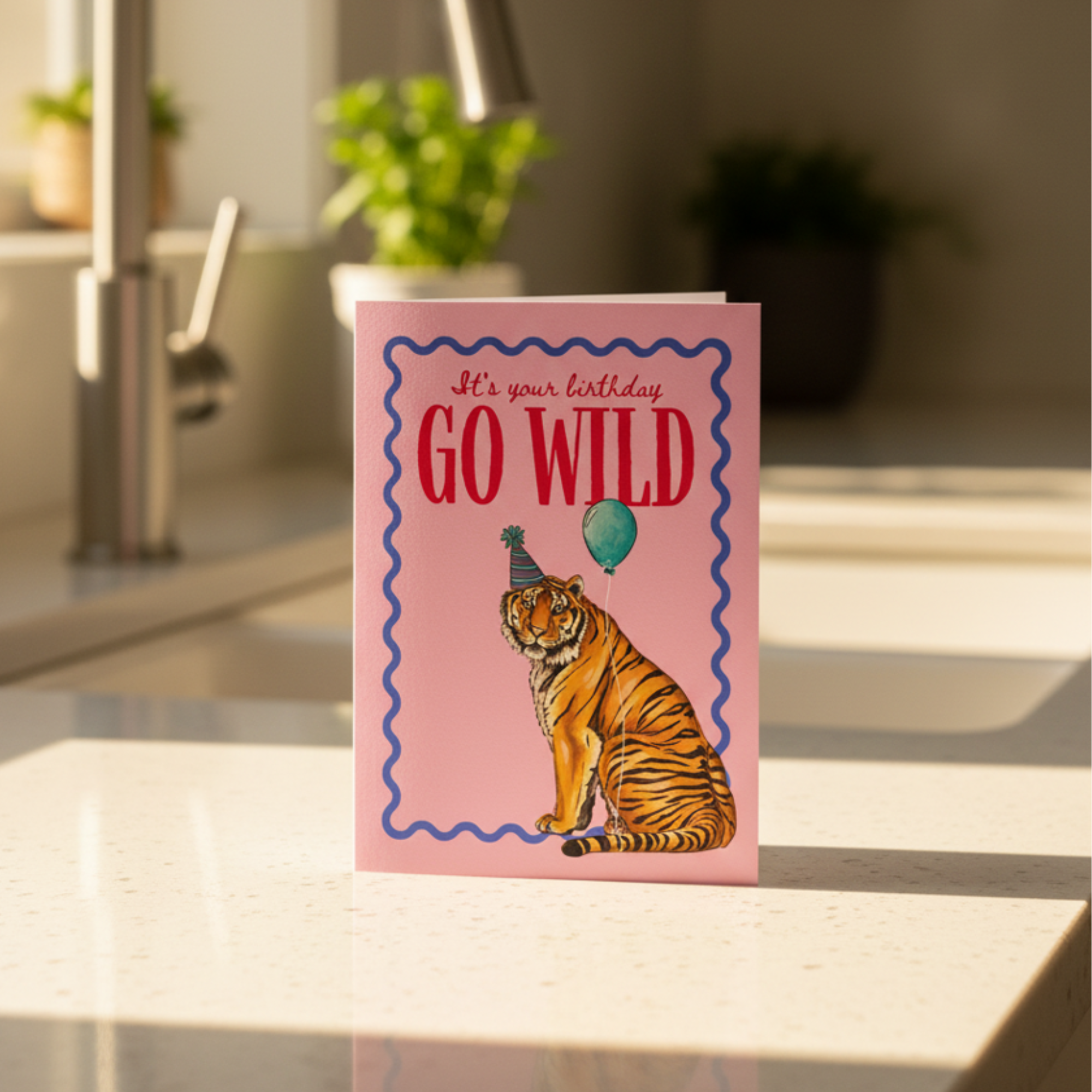Birthday card with a tiger illustration and 'Go Wild' text on a pink background, placed on a table.