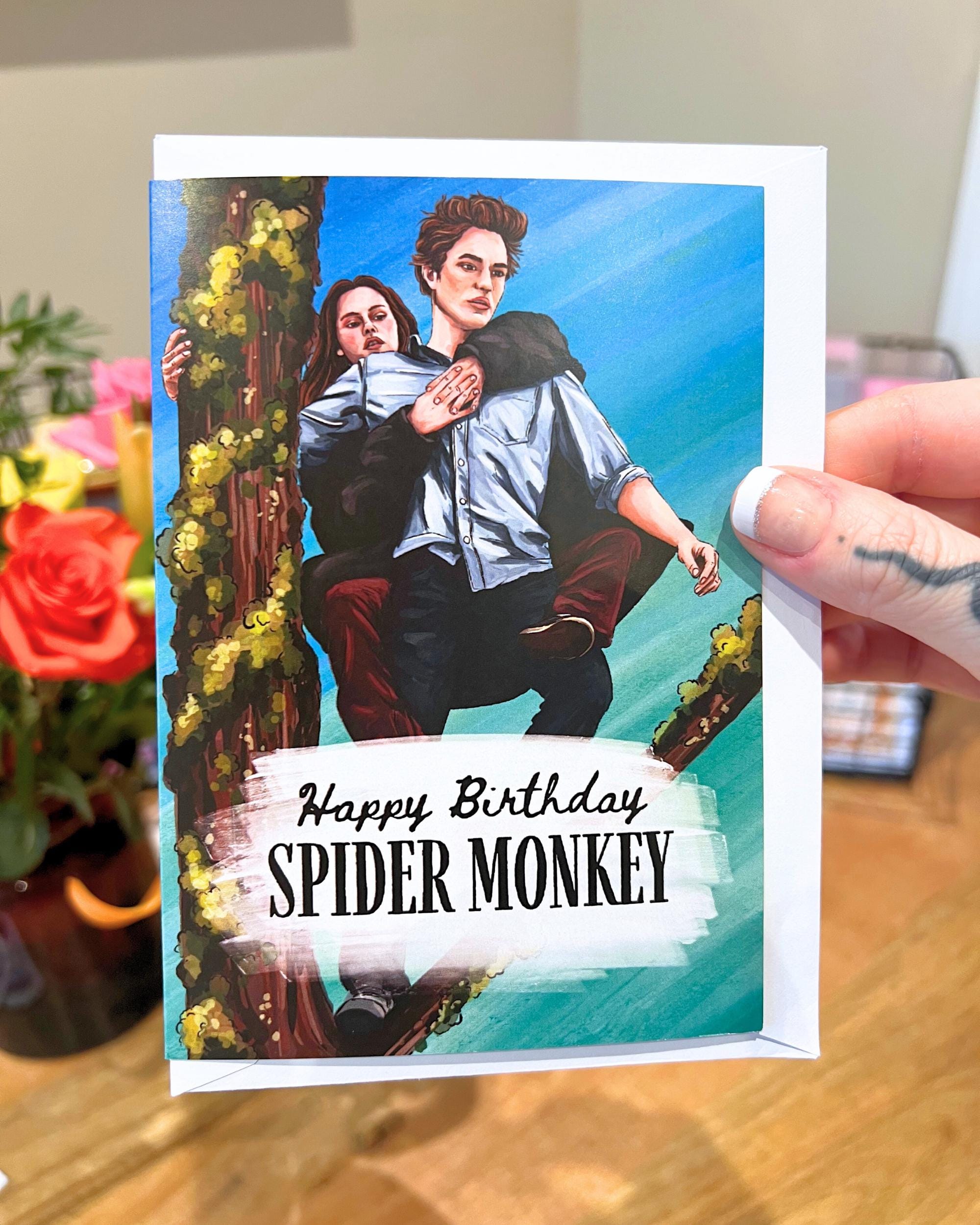 Birthday card with illustration of two people on a branch, text 'Happy Birthday SPIDER MONKEY', held by a hand.