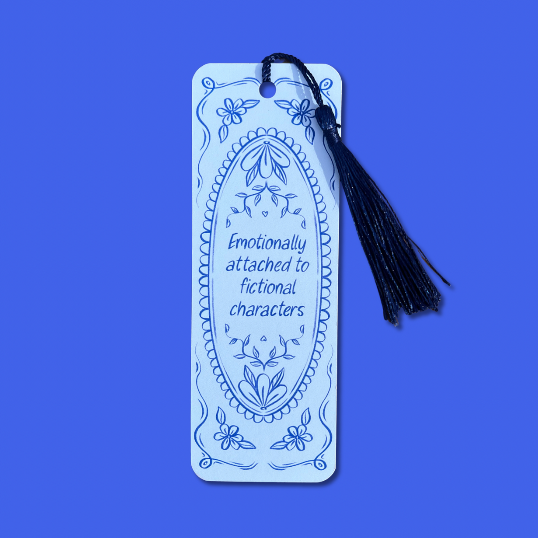 A light blue rectangular bookmark with a black tassel, featuring blue line-art floral designs and the printed text 'Emotionally attached to fictional characters' on a solid blue background.
