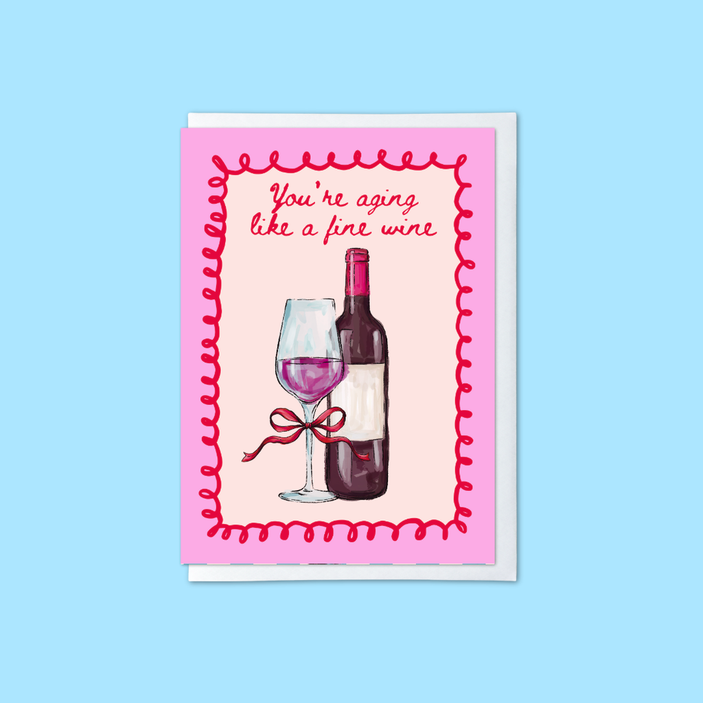 Pink and red birthday card with wine glass and bottle illustration and ‘you’re aging like a fine wine’ message
